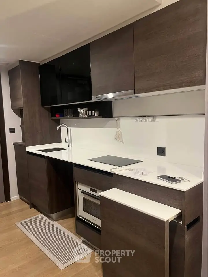 Modern kitchen with sleek dark cabinets and built-in oven, featuring a minimalist design and efficient layout.