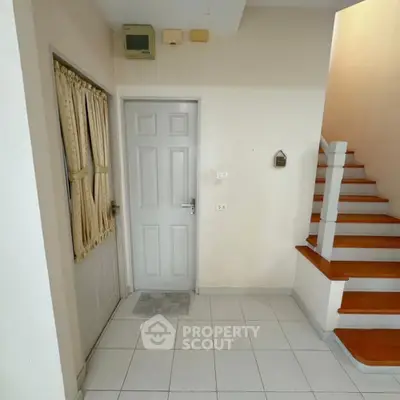 Bright and welcoming entryway with staircase leading to upper levels, featuring clean white tiles and a secure front door.