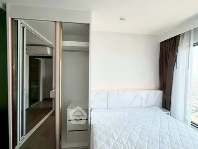 Modern bedroom with mirrored closet and large window offering city views.