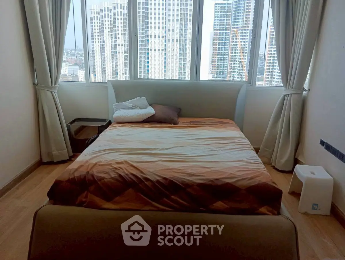 Spacious bedroom with city view and modern furnishings in high-rise apartment.