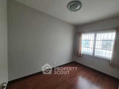 Spacious empty room with wooden flooring and large window, perfect for customization.