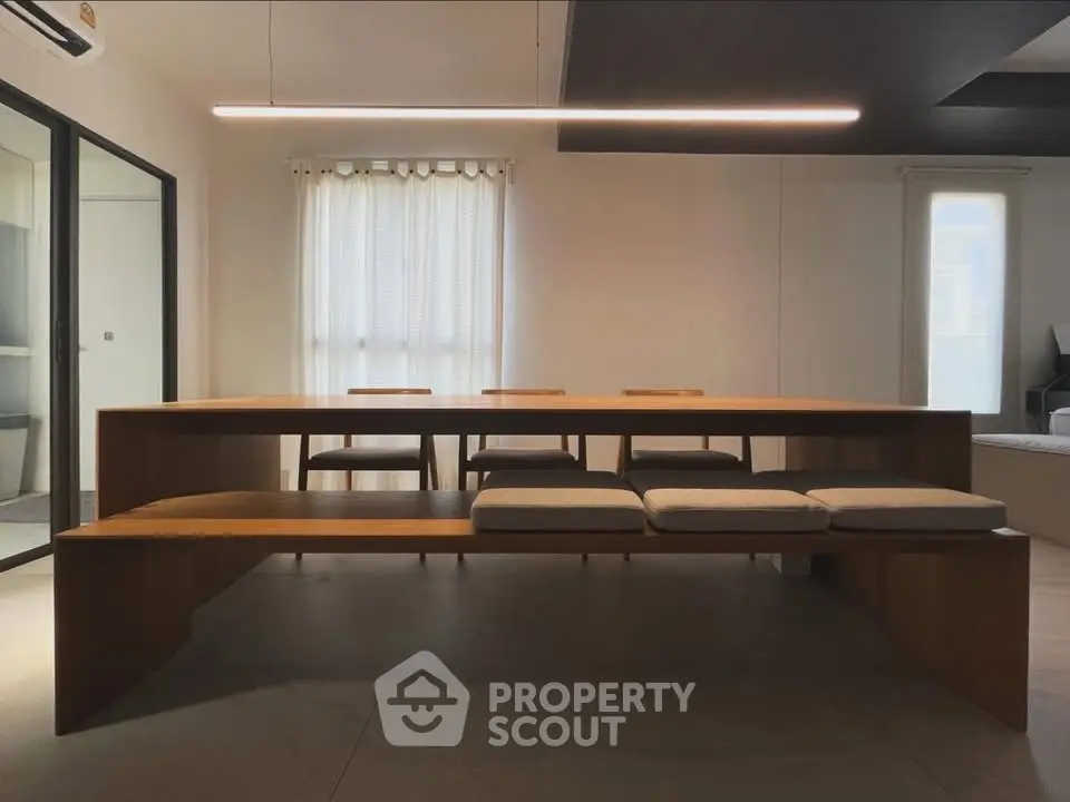 Modern dining area with sleek wooden table and cushioned benches, featuring minimalist design and natural light.