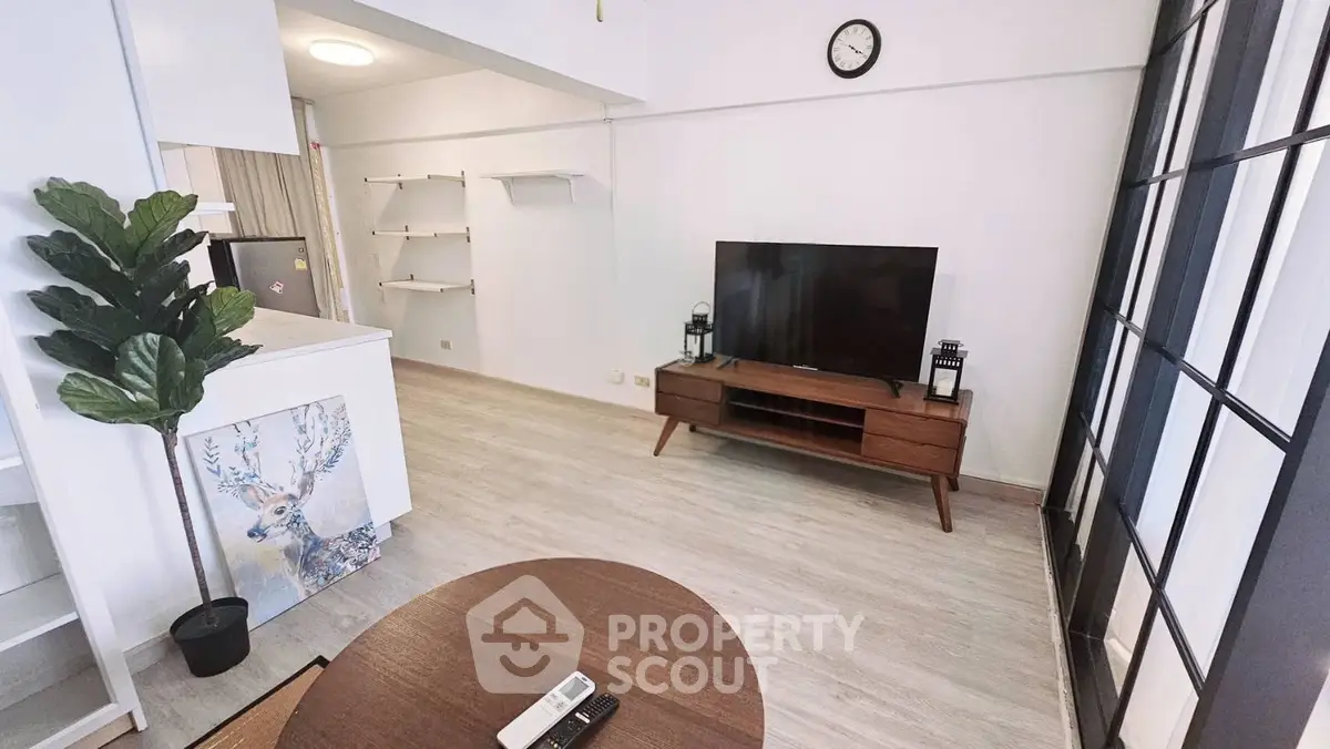 Modern living room with stylish decor, featuring a large TV, wooden furniture, and elegant shelving.