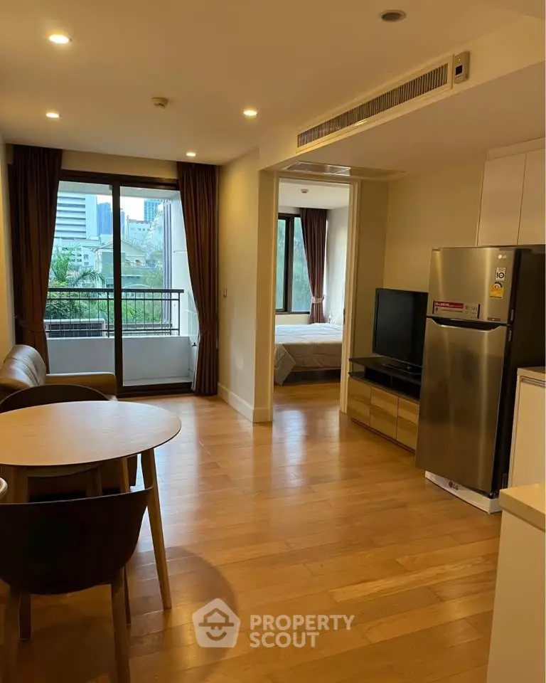 Modern open-plan living room with dining area and view of bedroom, featuring wooden flooring and natural light.