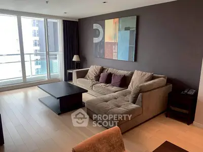 Spacious modern living room with large sofa and abstract art, featuring floor-to-ceiling windows for natural light.