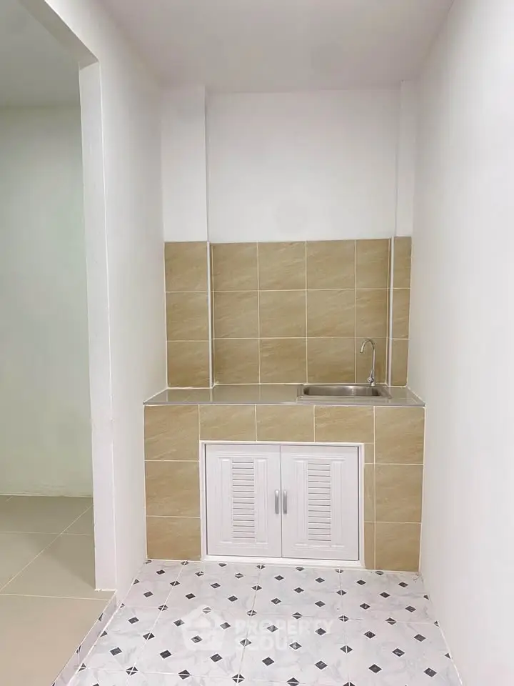 Compact kitchen area with tiled backsplash and single sink in modern apartment.
