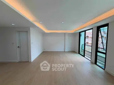 Spacious modern living room with large windows and balcony access, featuring elegant recessed lighting.