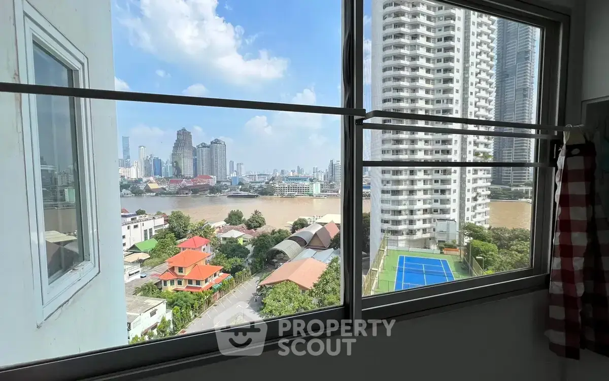 Stunning cityscape view from high-rise apartment window overlooking river and tennis court.