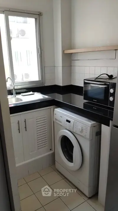 Compact kitchen with washing machine and microwave, ideal for urban living.