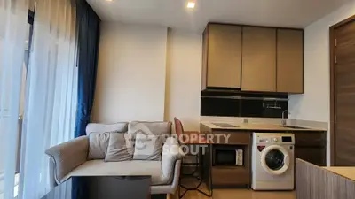 Modern living room with cozy sofa and stylish kitchen featuring washing machine and microwave.
