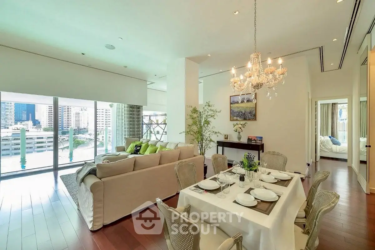 Luxurious open-plan living and dining area with elegant chandelier and city view.