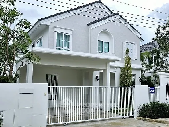 Elegant two-story white house with gated entrance and lush greenery.