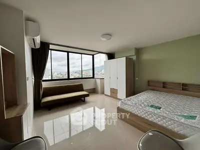 Spacious bedroom with large windows offering city views, modern furnishings, and ample natural light.