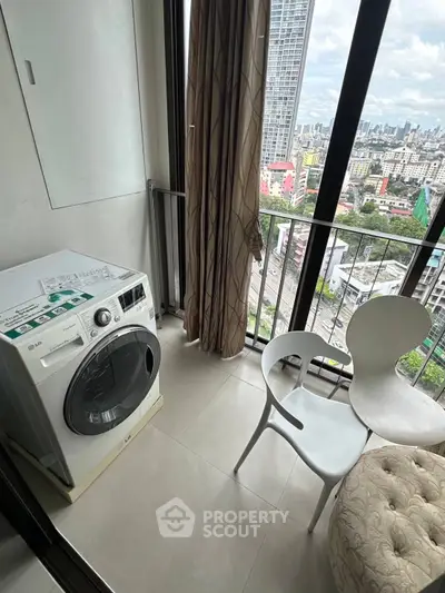 High-rise apartment balcony with city view, featuring a washing machine and modern seating area.