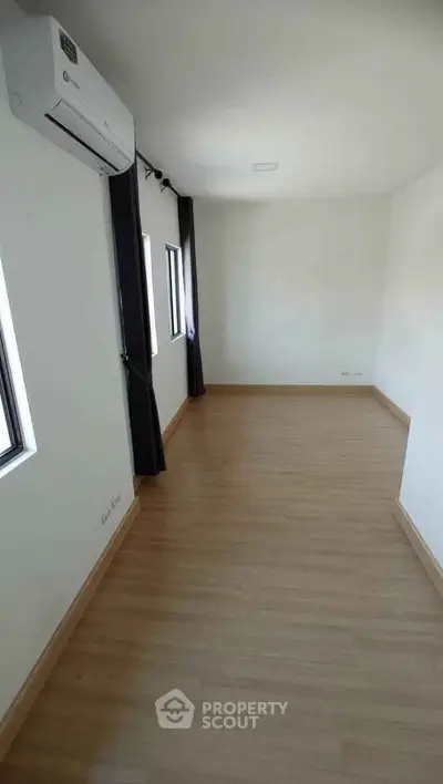 Spacious empty room with wooden flooring and air conditioning, ready for customization.