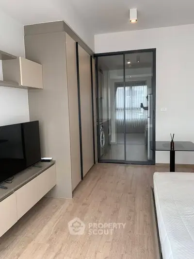 Modern studio apartment with sleek design, featuring a glass partition and built-in storage solutions.