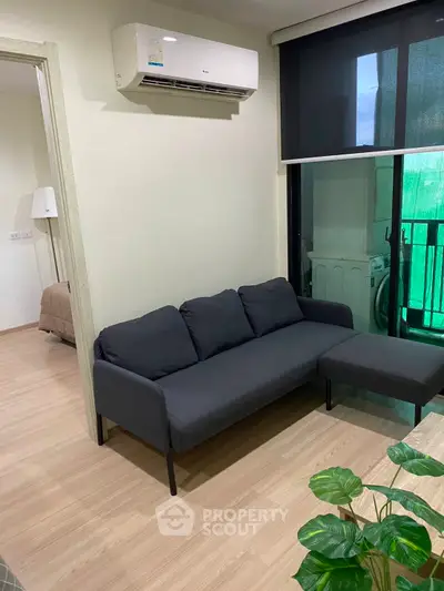 Modern living room with sleek black sofa and air conditioning, adjacent to a cozy bedroom and balcony.