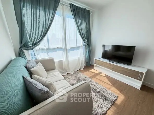 Bright living room with modern sofa, TV, and large windows with sheer curtains.