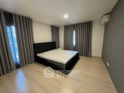 Spacious bedroom with modern design and natural light, featuring a comfortable bed and elegant curtains.