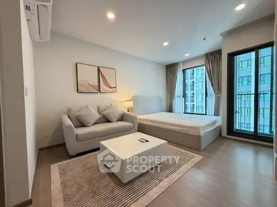 Modern bedroom with cozy seating area and large window view in stylish apartment.