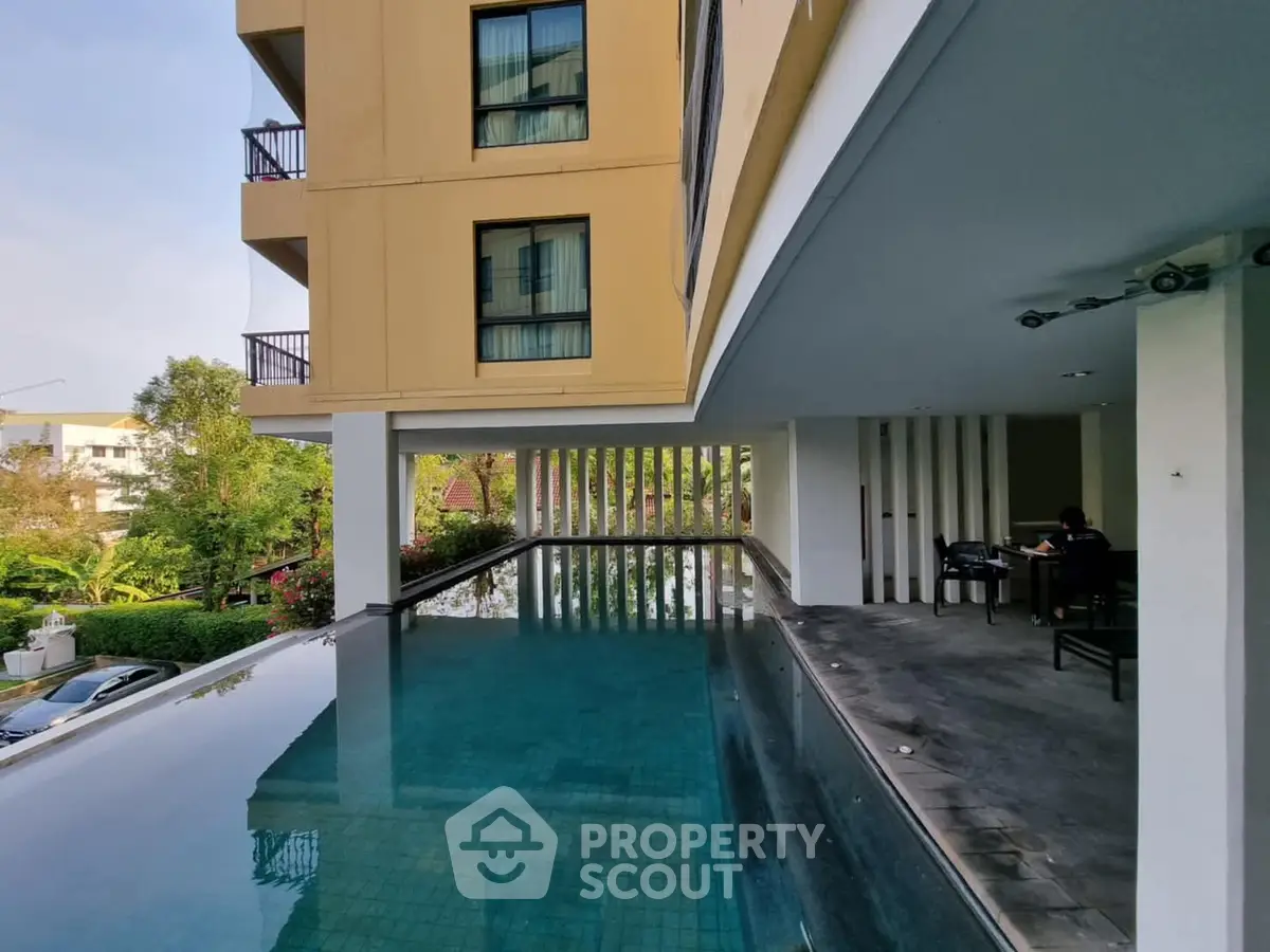 Luxurious apartment building with serene poolside view and modern architecture.
