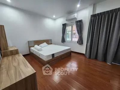 Spacious bedroom with wooden flooring and modern furnishings in a well-lit apartment.