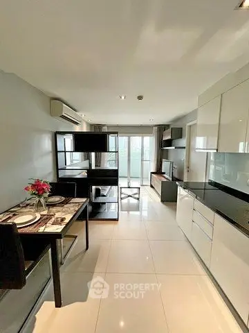 Modern open-plan living room with sleek kitchen and dining area, featuring large windows and stylish decor.