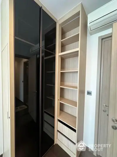 Modern storage space with sleek black glass doors and open shelving in a contemporary home.