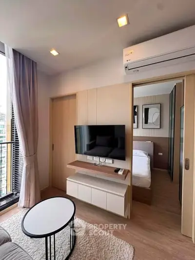 Modern living room with sleek design, featuring a wall-mounted TV, air conditioning, and a glimpse into a cozy bedroom.
