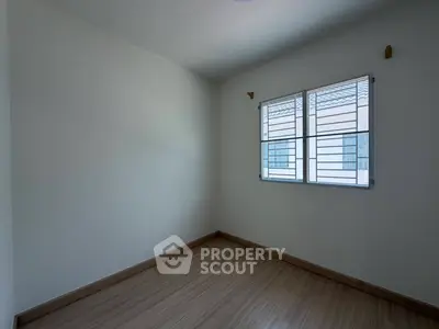 Spacious empty room with wooden flooring and large window, perfect for customization.