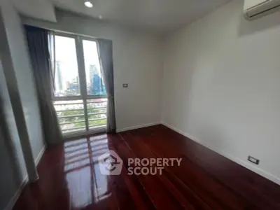 Spacious bedroom with polished wooden floors and large window offering city views.