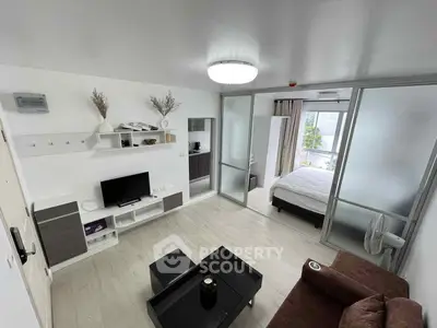 Modern living room with open layout and bedroom view, featuring sleek furniture and natural light.