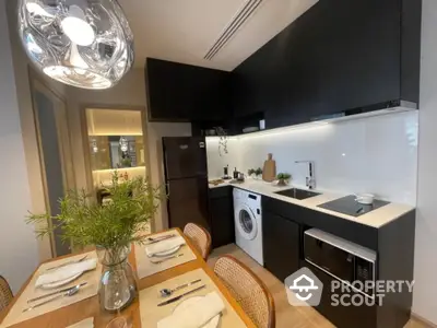 Modern kitchen with sleek black cabinetry and high-end appliances, including a built-in oven and washing machine, complemented by a stylish dining area.