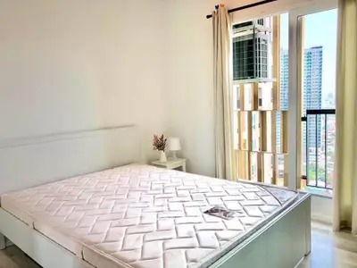 Bright bedroom with large window and city view, featuring a comfortable bed and minimalist decor.