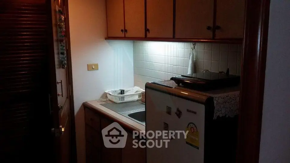 Cozy compact kitchen with wooden cabinets and small fridge, ideal for efficient space use.
