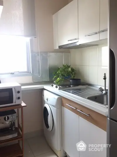 Compact kitchen with washing machine and microwave, ideal for small apartments.