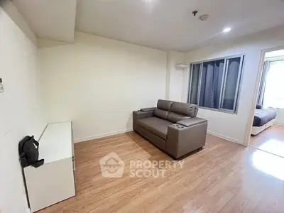 Cozy living room with modern sofa and wooden flooring, adjacent to a bedroom.