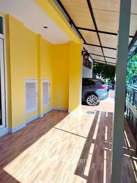 Spacious covered parking area with wooden flooring and vibrant yellow walls.