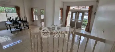 Spacious living room with natural light and garden view, featuring tiled floors and elegant staircase.