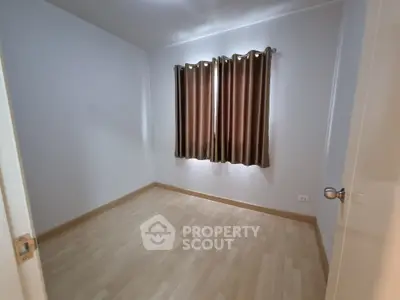 Spacious empty bedroom with wooden flooring and brown curtains