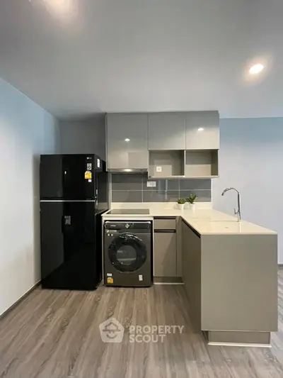 Modern kitchen with sleek cabinets, fridge, and washing machine in open layout.