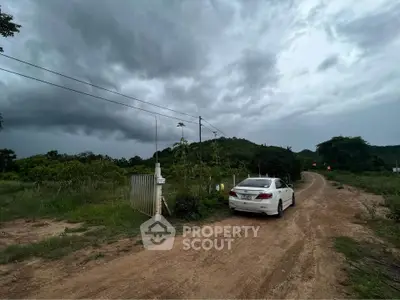 Scenic rural property entrance with car and lush greenery under dramatic skies.