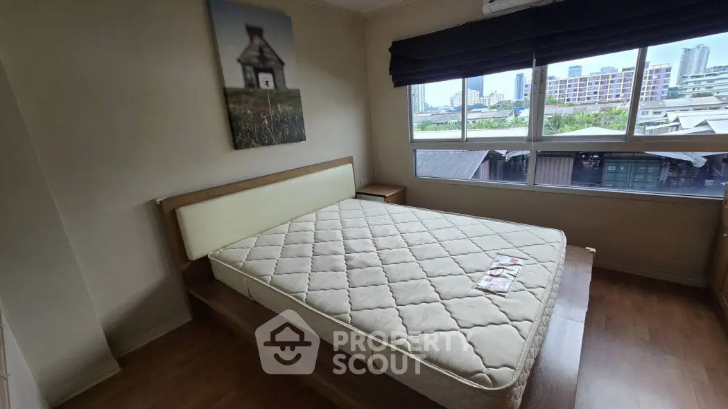 Spacious bedroom with large window and city view, featuring a comfortable bed and wooden flooring.