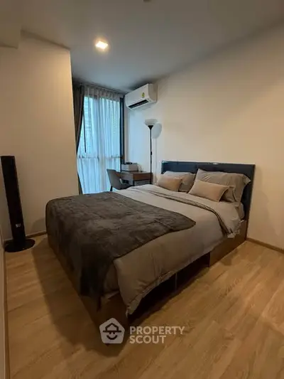 Cozy modern bedroom with wooden flooring and large window, featuring a comfortable bed and stylish decor.