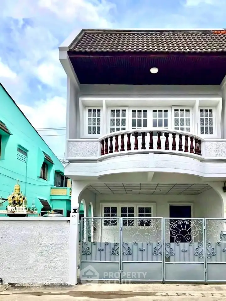 Charming two-story house with elegant balcony and gated entrance in a serene neighborhood.