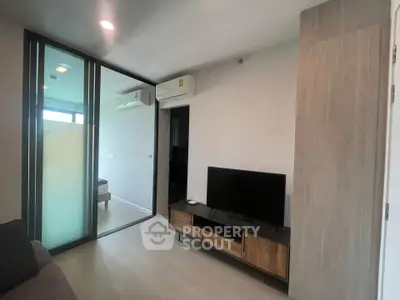 Modern living room with sleek design, featuring a TV stand and glass partition leading to a bedroom.