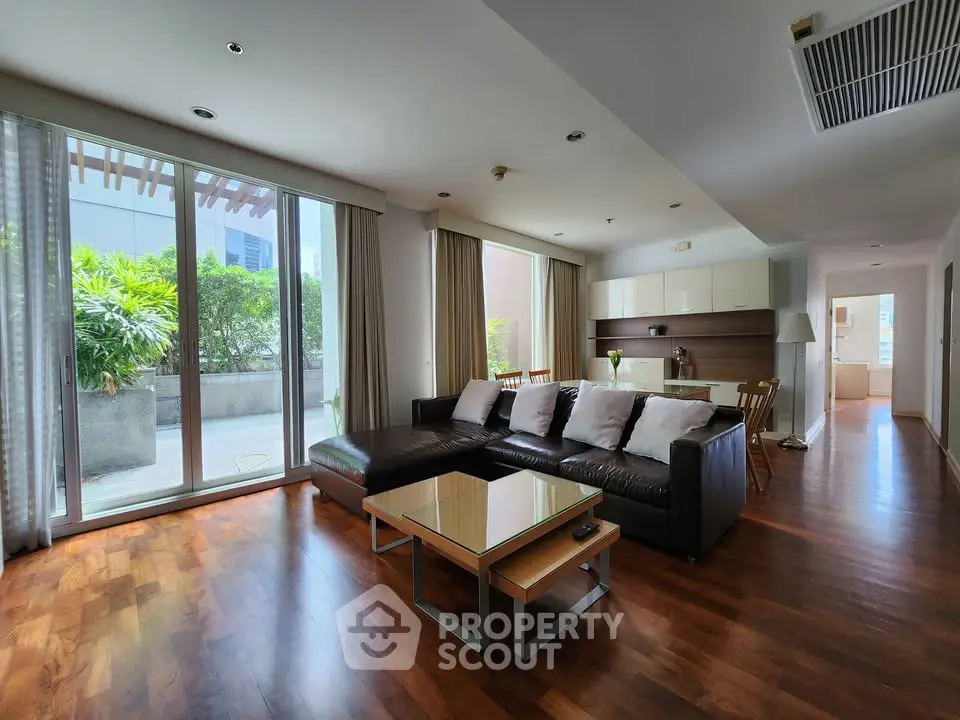 Spacious living room with large windows and garden view, featuring modern furniture and wooden flooring.