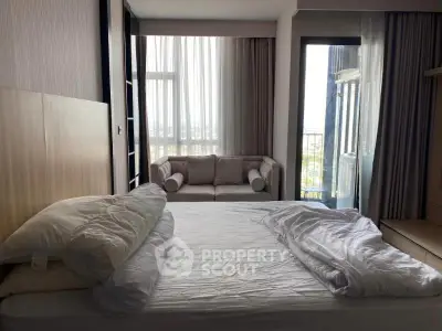 Spacious bedroom with large windows and balcony access, featuring a cozy sofa and modern decor.