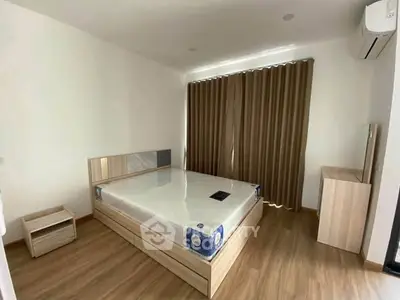 Spacious bedroom with modern wooden flooring and large window with curtains.