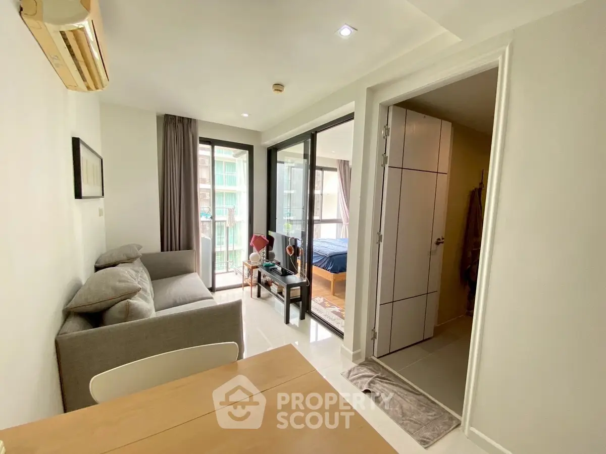 Modern apartment interior with open living room and bedroom, featuring sleek furniture and natural light.